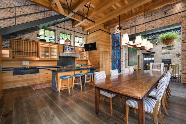 dining space with dark wood-type flooring, beamed ceiling, a high ceiling, and an outdoor fireplace