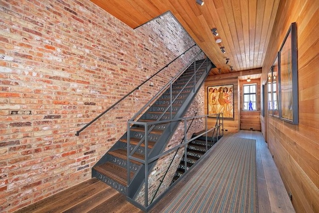 stairway featuring wood ceiling, wood walls, brick wall, and wood finished floors