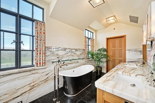 bathroom featuring a freestanding tub, a sink, visible vents, tile walls, and vaulted ceiling