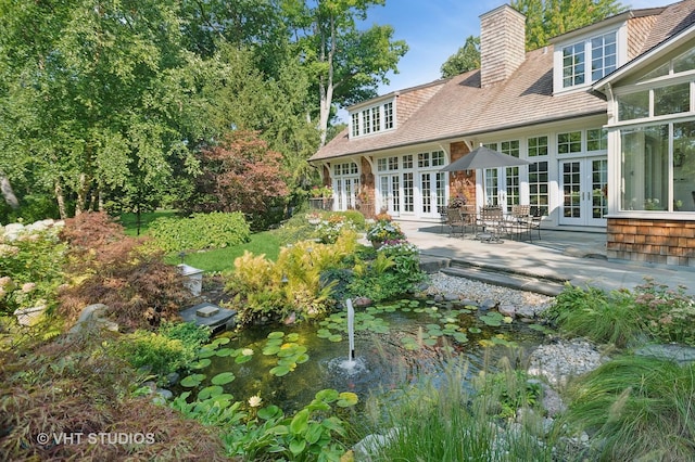 rear view of property featuring a patio area, a garden pond, french doors, and a chimney