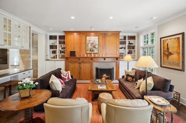 living room with built in shelves, ornamental molding, wood finished floors, recessed lighting, and a lit fireplace