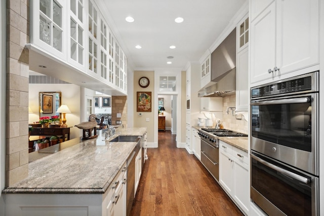 kitchen featuring backsplash, appliances with stainless steel finishes, white cabinets, and wall chimney range hood