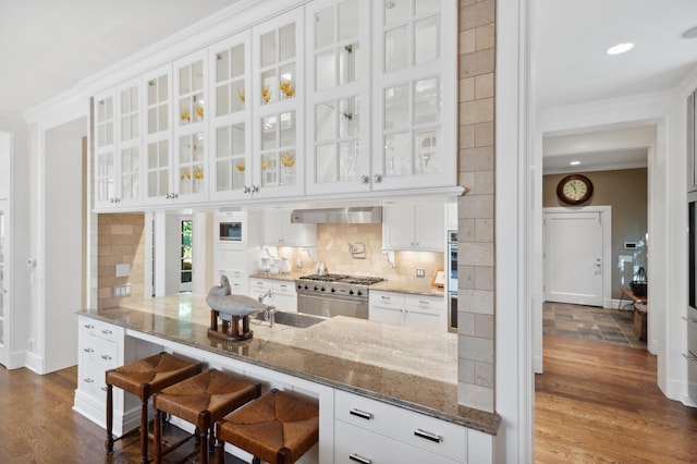 kitchen featuring dark stone counters, ornamental molding, white cabinets, wall chimney range hood, and tasteful backsplash