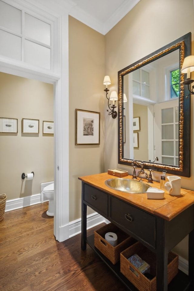 bathroom with toilet, wood finished floors, crown molding, baseboards, and vanity