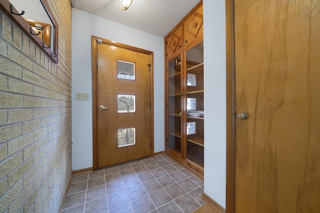 doorway with baseboards and dark tile patterned flooring