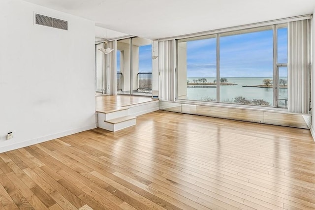 empty room with visible vents, baseboards, a water view, and hardwood / wood-style flooring