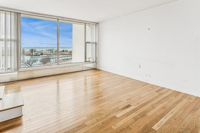 unfurnished room featuring hardwood / wood-style flooring, baseboards, and a water view