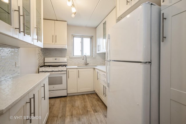 kitchen featuring white appliances, a sink, white cabinetry, light wood finished floors, and tasteful backsplash