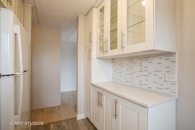 kitchen with glass insert cabinets, decorative backsplash, wood finished floors, and freestanding refrigerator