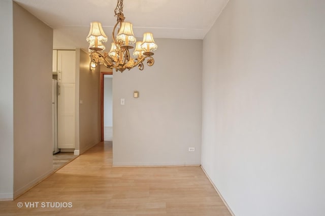 unfurnished room with a chandelier, light wood-style flooring, and baseboards