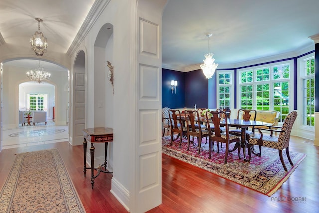 dining space with arched walkways, an inviting chandelier, ornamental molding, wood finished floors, and baseboards