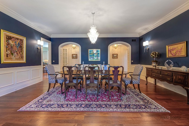 dining room featuring arched walkways, ornamental molding, a wainscoted wall, and wood finished floors