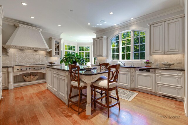 kitchen with stainless steel gas cooktop, a kitchen island, ornamental molding, light wood-type flooring, and custom range hood