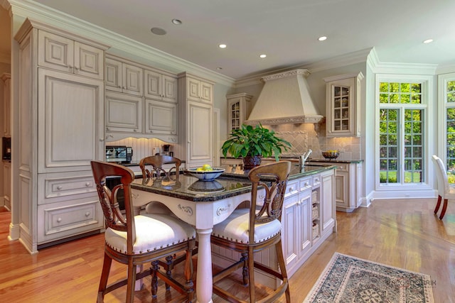 kitchen with glass insert cabinets, a breakfast bar, cream cabinetry, and custom range hood