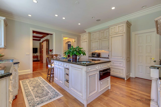 kitchen with light wood finished floors, dark stone counters, cream cabinetry, a sink, and a warming drawer