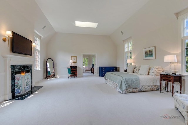 carpeted bedroom featuring a skylight, a premium fireplace, high vaulted ceiling, and multiple windows