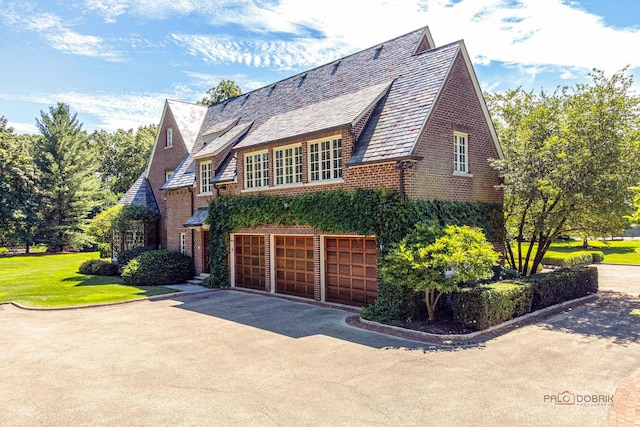 view of front of home featuring driveway, brick siding, an attached garage, a high end roof, and a front yard