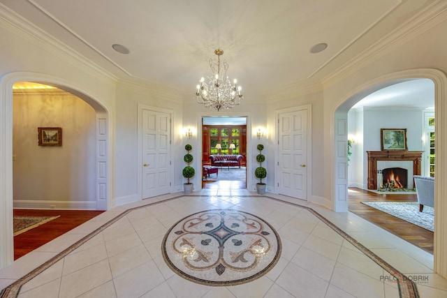 foyer entrance with arched walkways, light tile patterned floors, a premium fireplace, ornamental molding, and baseboards