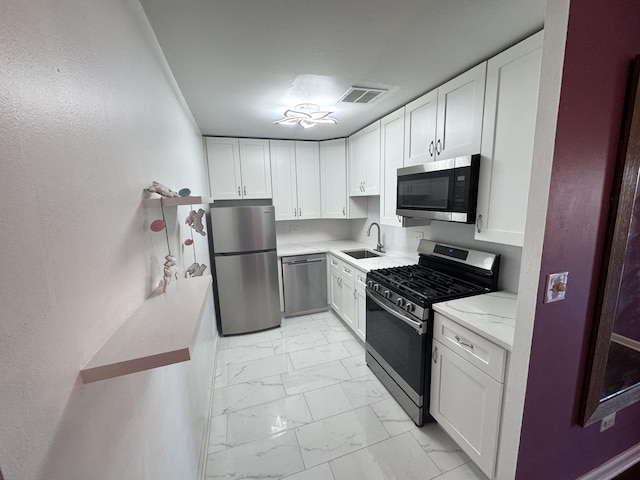 kitchen featuring visible vents, marble finish floor, stainless steel appliances, white cabinetry, and a sink