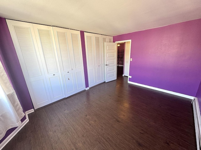 unfurnished bedroom with dark wood finished floors, baseboards, and two closets