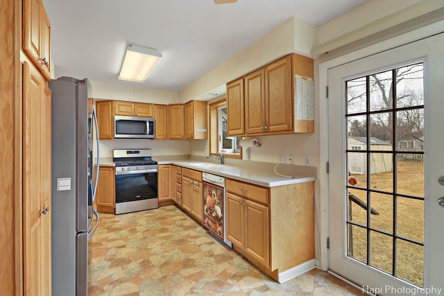 kitchen with light countertops, appliances with stainless steel finishes, a sink, and stone finish flooring