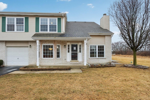 view of front of home featuring a front lawn, a chimney, brick siding, and aphalt driveway