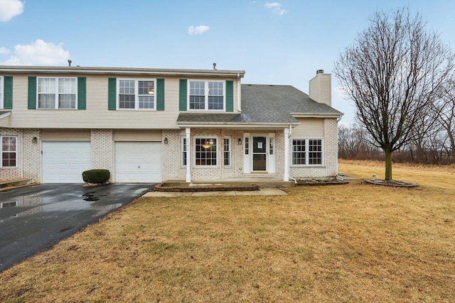 view of front of house featuring aphalt driveway, brick siding, a front lawn, and a chimney