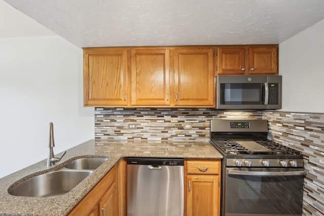 kitchen featuring a sink, tasteful backsplash, stainless steel appliances, brown cabinetry, and light stone countertops