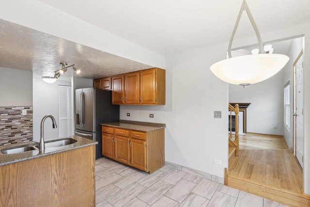 kitchen with wood finish floors, brown cabinets, a sink, dark stone countertops, and decorative backsplash