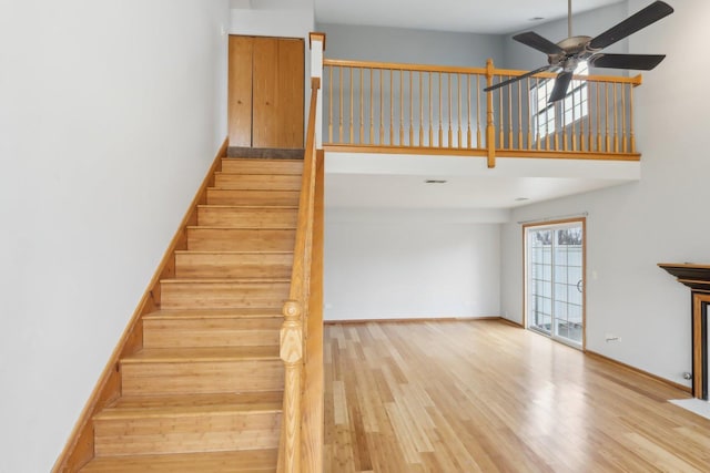 staircase featuring baseboards, a ceiling fan, wood finished floors, and a towering ceiling