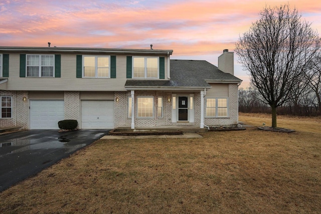 view of front facade featuring aphalt driveway, a lawn, brick siding, and a chimney