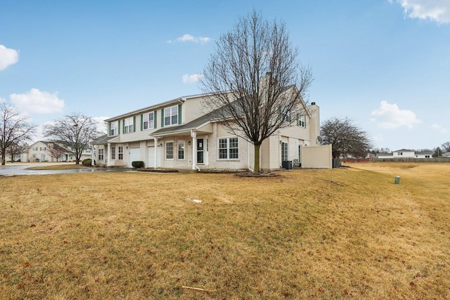 traditional-style home featuring brick siding, cooling unit, an attached garage, and a front lawn