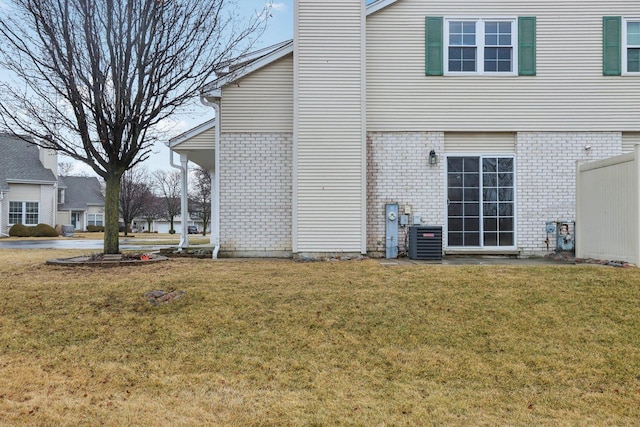 rear view of house featuring a yard, brick siding, central AC unit, and a chimney