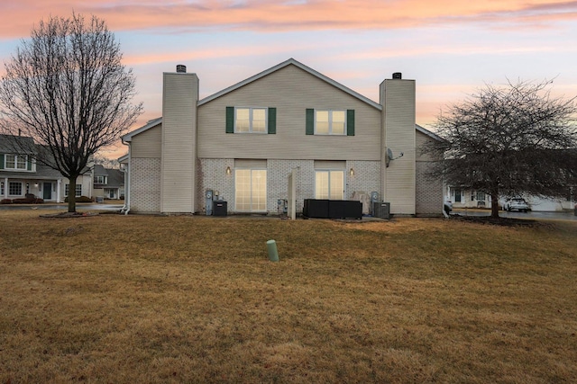 back of house at dusk featuring a lawn, central AC, and a chimney