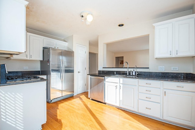 kitchen with a sink, white cabinetry, light wood-style floors, appliances with stainless steel finishes, and dark stone countertops