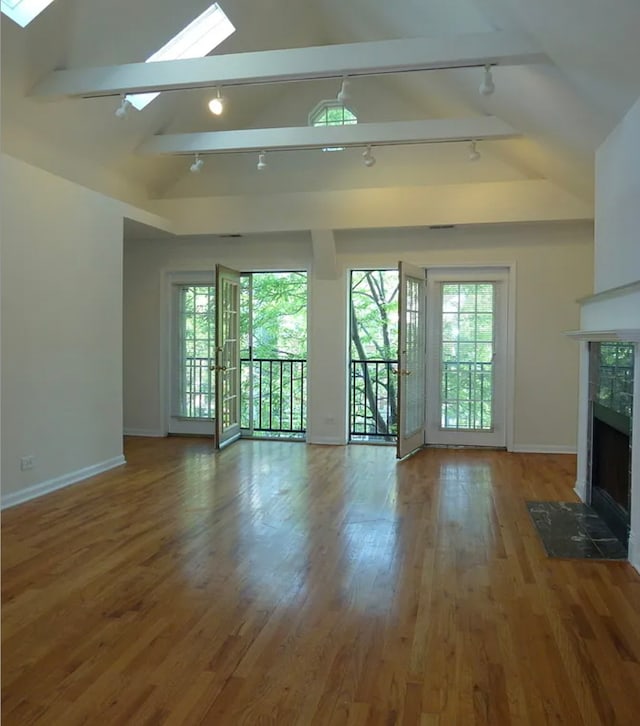 unfurnished living room with a tile fireplace, vaulted ceiling with skylight, baseboards, and wood finished floors