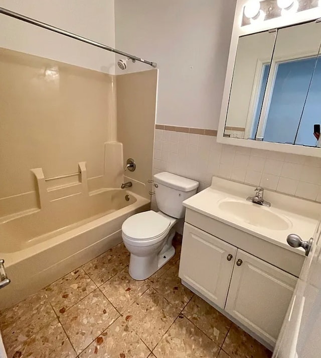 full bath with shower / washtub combination, tile walls, toilet, wainscoting, and vanity