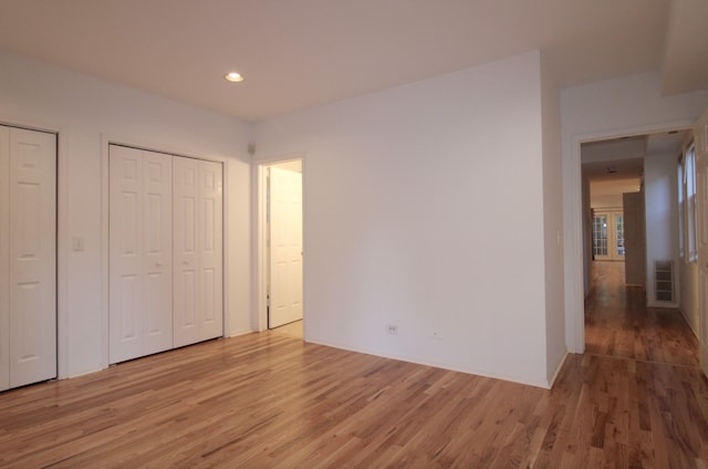 unfurnished bedroom with light wood-type flooring, visible vents, two closets, and recessed lighting