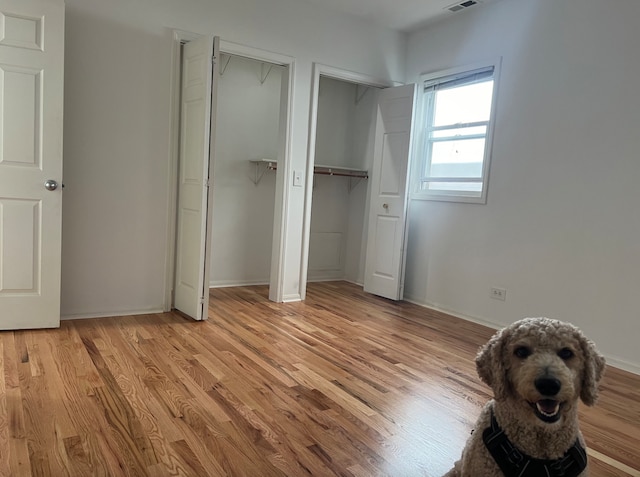 unfurnished bedroom with baseboards, light wood finished floors, visible vents, and multiple closets