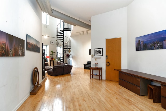 corridor featuring stairs, a high ceiling, light wood-style flooring, and track lighting