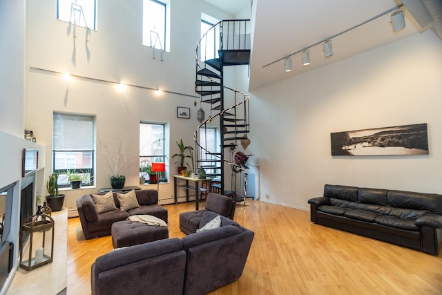 living area with a baseboard radiator, stairway, a fireplace with raised hearth, and wood finished floors