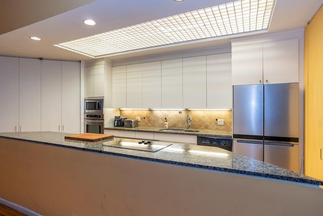 kitchen featuring stainless steel appliances, decorative backsplash, white cabinets, a sink, and dark stone counters