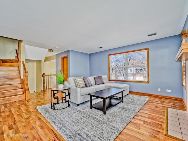 living area featuring stairs, baseboards, visible vents, and light wood finished floors