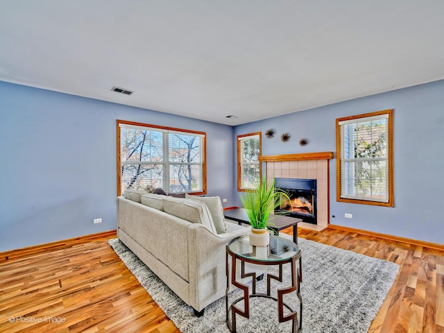 living area with visible vents, a tile fireplace, baseboards, and wood finished floors