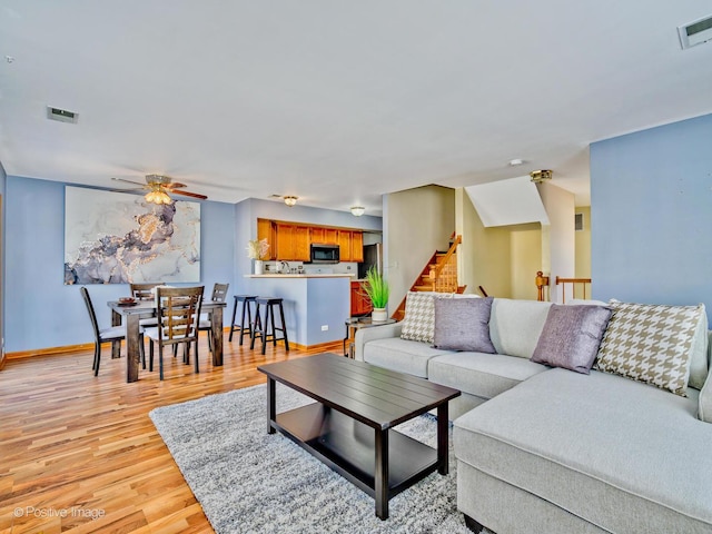 living area with stairway, light wood-style flooring, baseboards, and visible vents