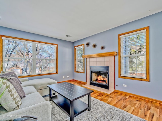 living room with visible vents, baseboards, wood finished floors, and a tiled fireplace