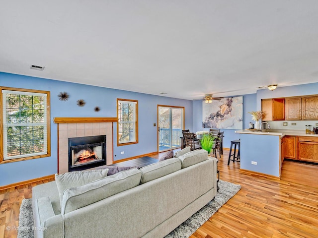 living room with light wood-type flooring, visible vents, baseboards, ceiling fan, and a tile fireplace