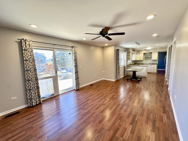 unfurnished living room with baseboards, visible vents, and dark wood-type flooring