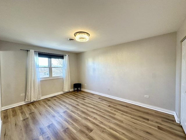 empty room with wood finished floors, visible vents, and baseboards