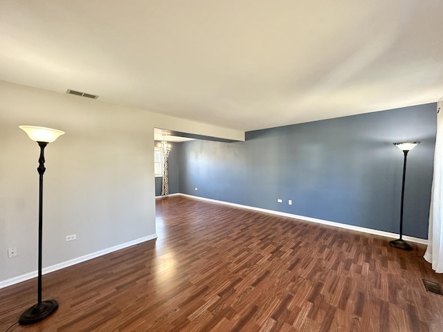 spare room featuring baseboards, visible vents, a chandelier, and dark wood-style flooring